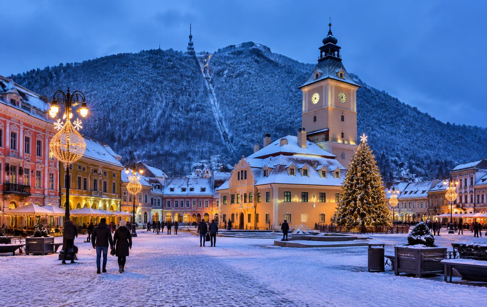 Council Square in Brașov covered in snow with festive lights at dusk